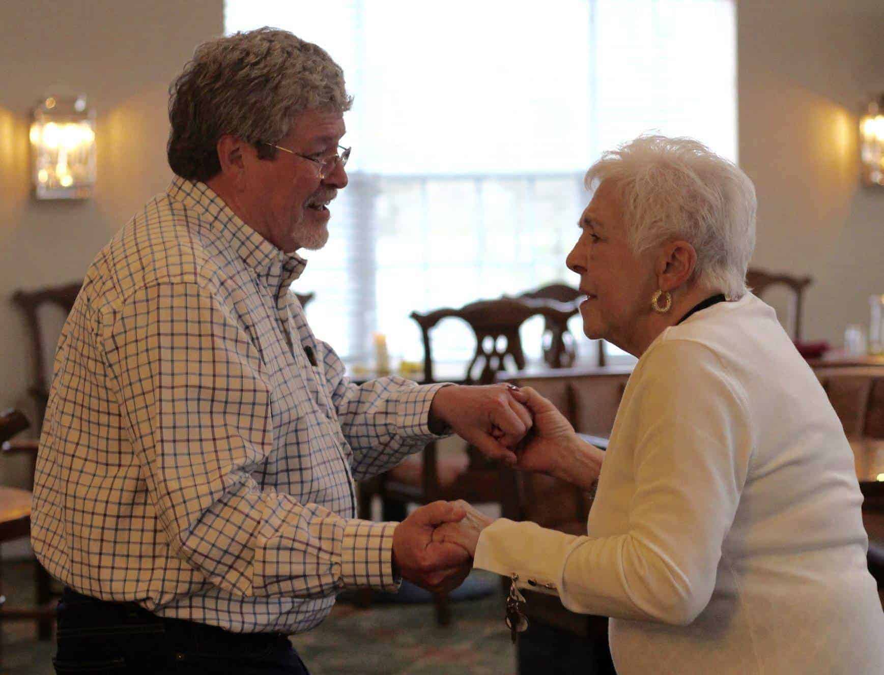 An older man holds hands with and older woman as they dance in the hall