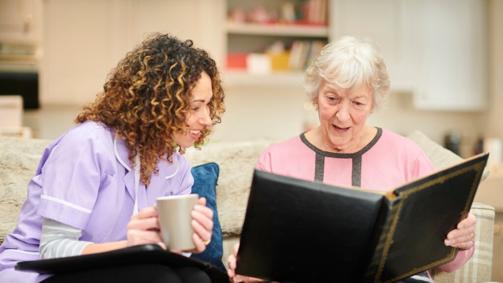 An older woman in pink is reading a book while the younger woman in purple looks over