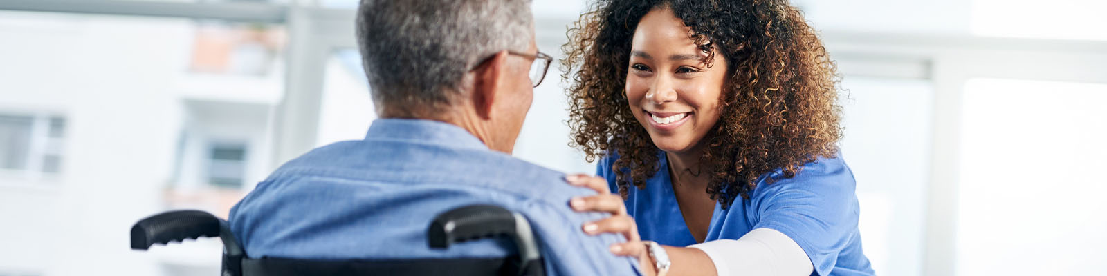 A senior man sitting in a wheelchair looking at his female nursing assistant